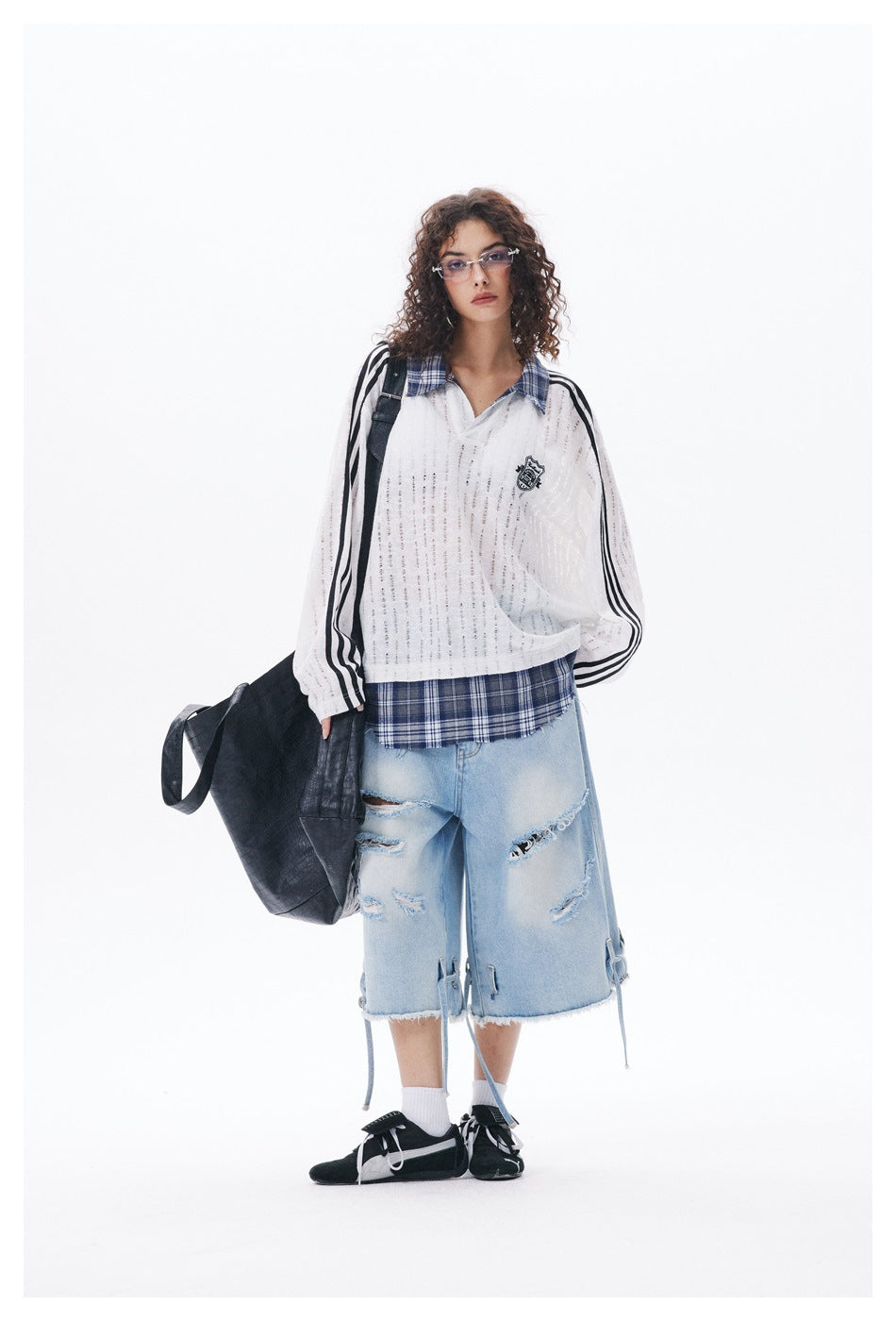 Model wearing the white striped-sleeve plaid-trim top with distressed denim shorts, black sneakers and a large black bag