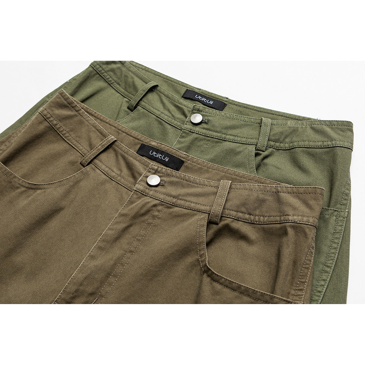 Close-up of olive-green and brown-olive pants showing front pockets, belt loops, buttons, and sewn-in labels.