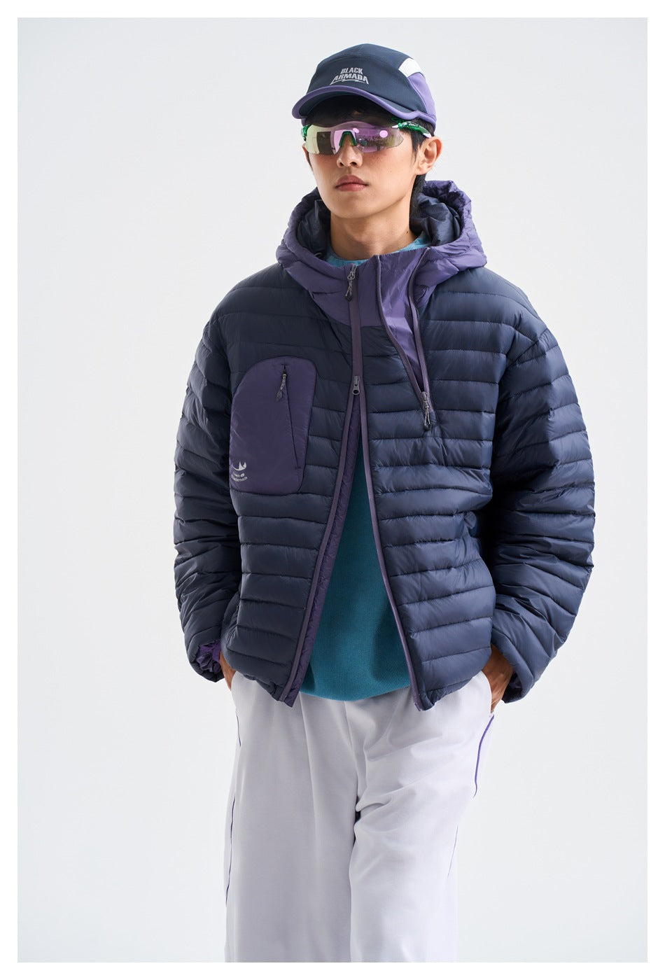 Front view of a person wearing a navy quilted jacket with purple hood and chest pocket, styled with white trousers.