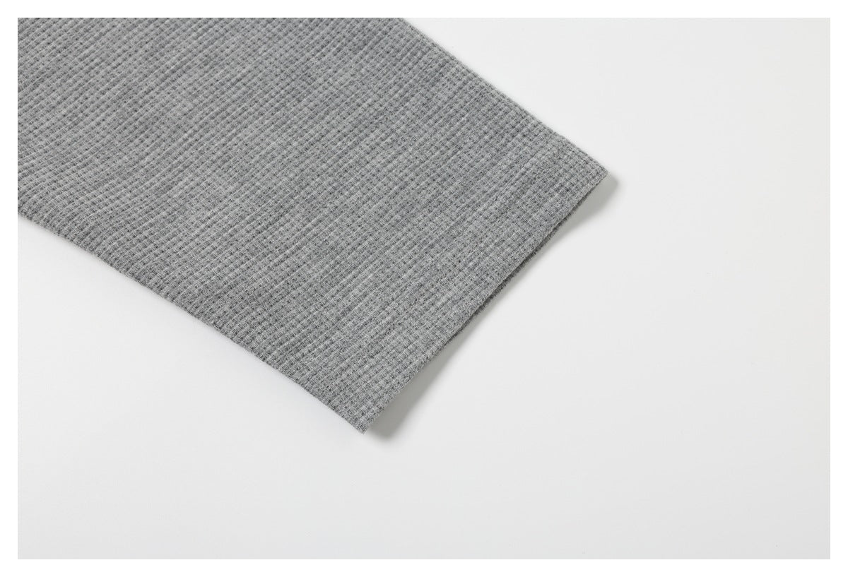 Close-up of the plain gray waffle-knit fabric and finished edge of a garment.