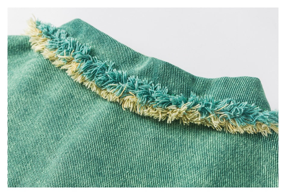 Close-up of a teal denim edge finished with shaggy teal and pale-yellow fringing.
