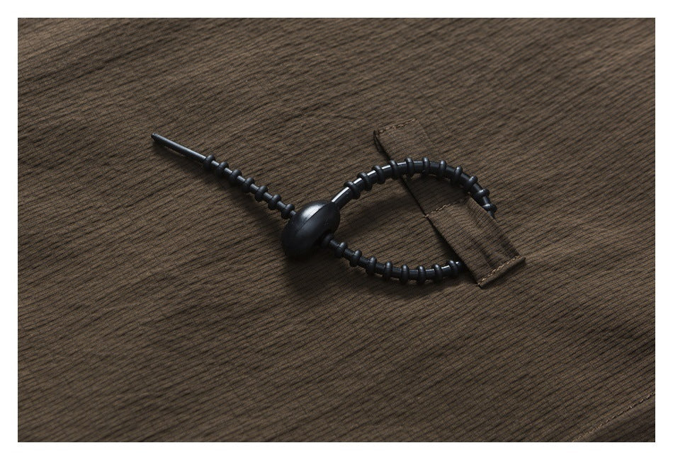 Black adjustable cord toggle and fabric tab shown against dark brown striped shirt fabric.