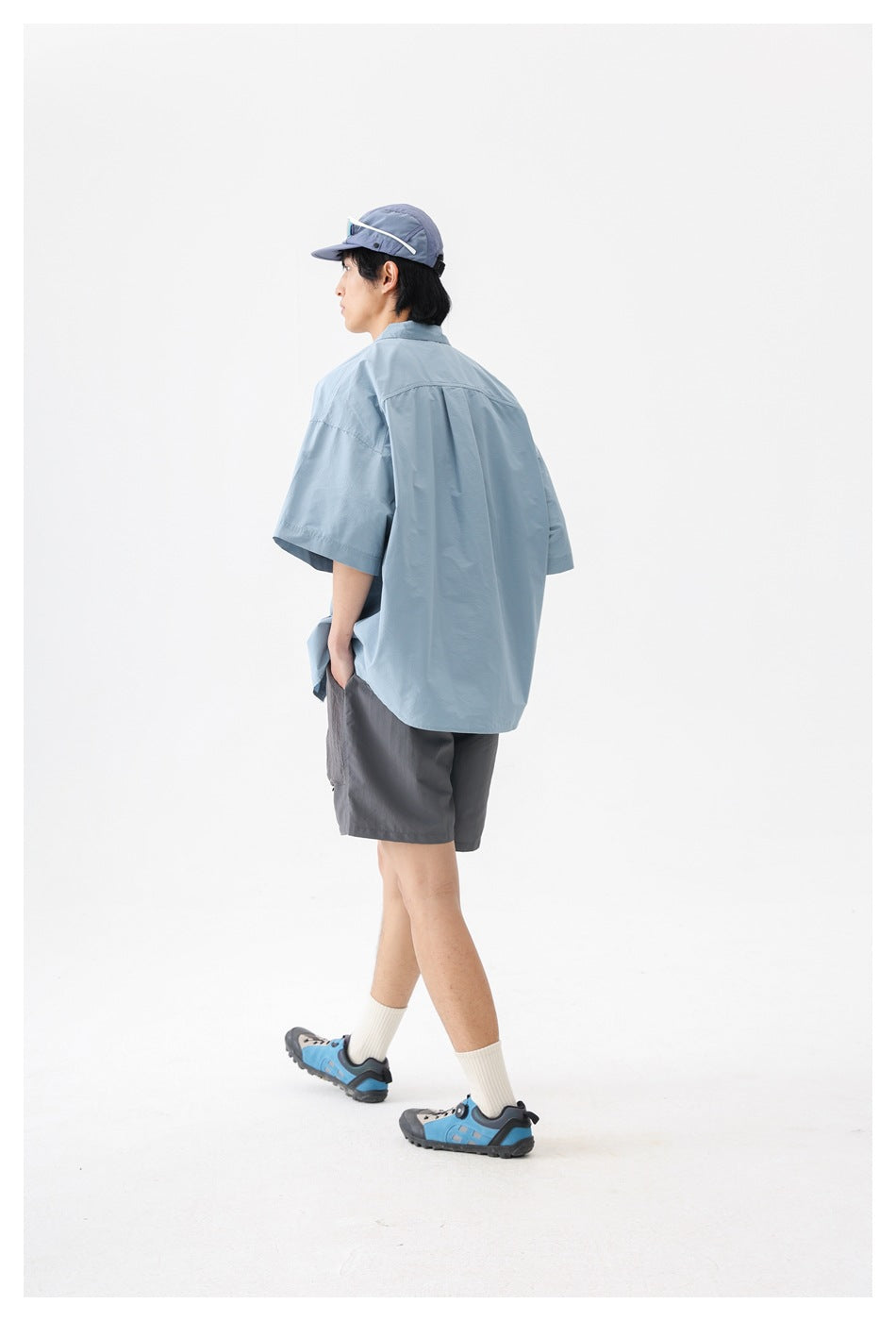 Model wearing a pale blue oversized short-sleeve shirt, shown from the back.