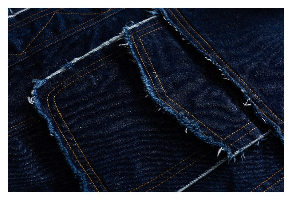 Close-up of dark indigo denim pocket panels with gold stitching and raw, frayed edges.