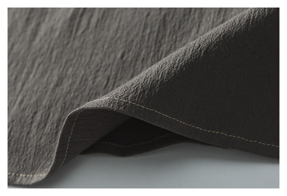 Close-up of a folded garment edge with light stitching on dark charcoal fabric.