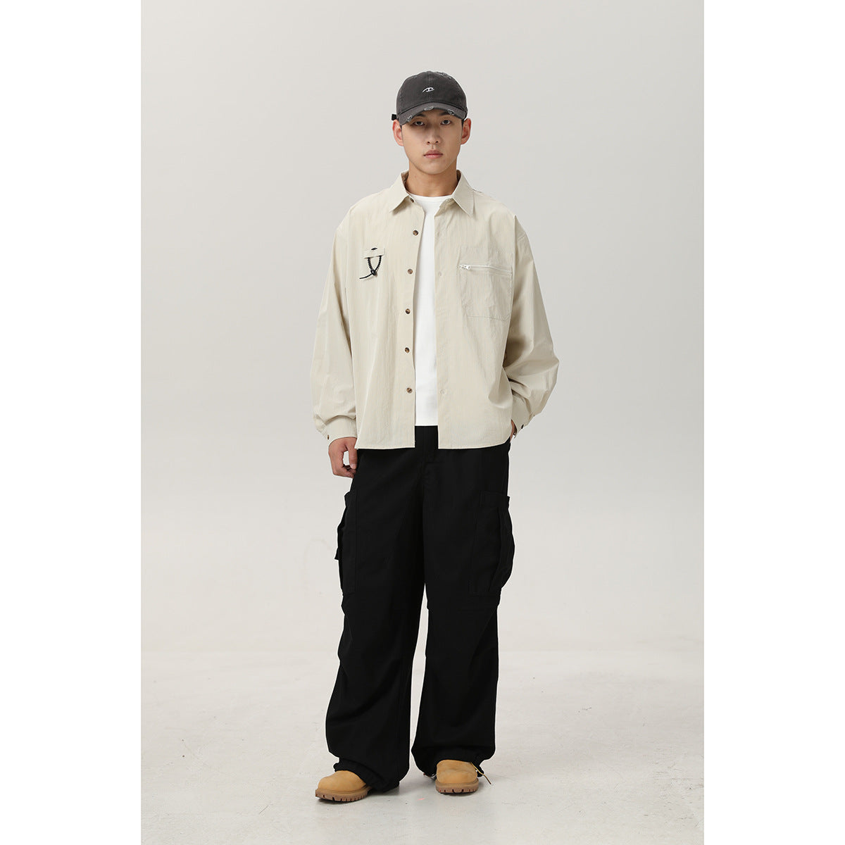 Model wearing a light beige button-front shirt with chest pockets and black cargo pants, shown full length.