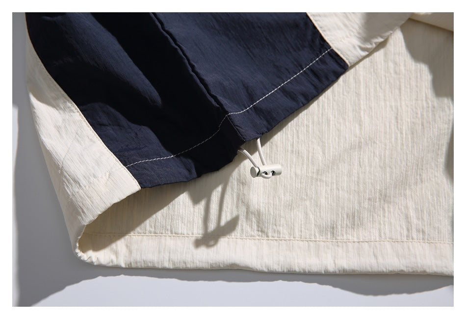 Close-up of an ivory and navy color-block garment hem with a white drawcord and toggle.