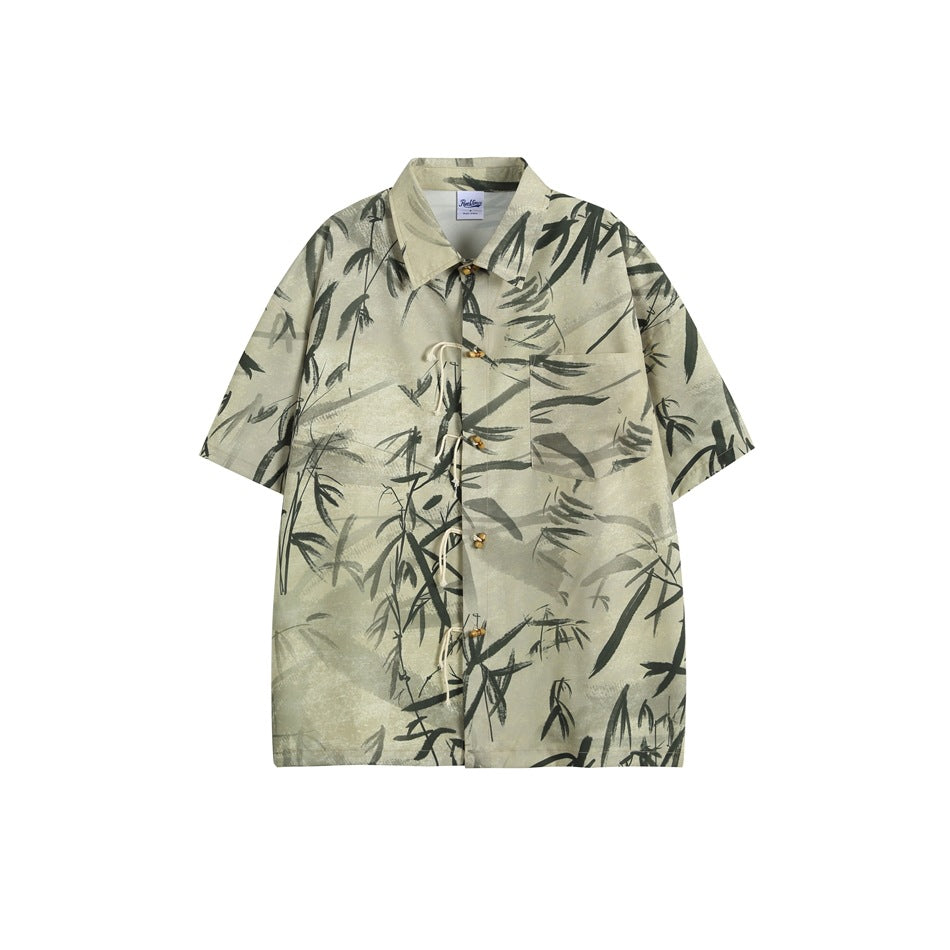 Flat-lay front of a beige short-sleeve shirt with a dark bamboo-leaf print, rope-loop toggle closure and chest pocket