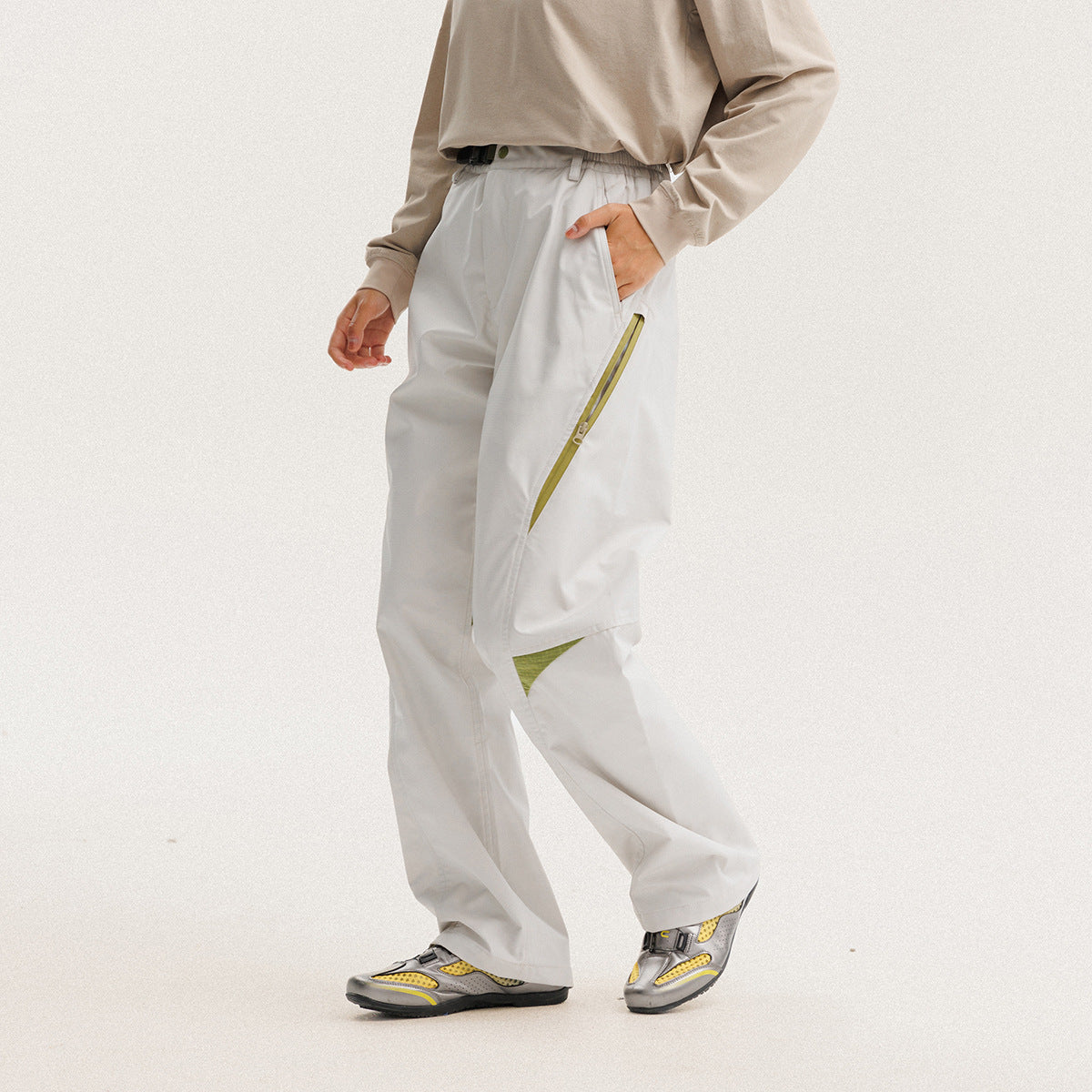 Model wearing loose white trousers with an elastic waist, angled lime-green zip detail and contrasting knee inserts.