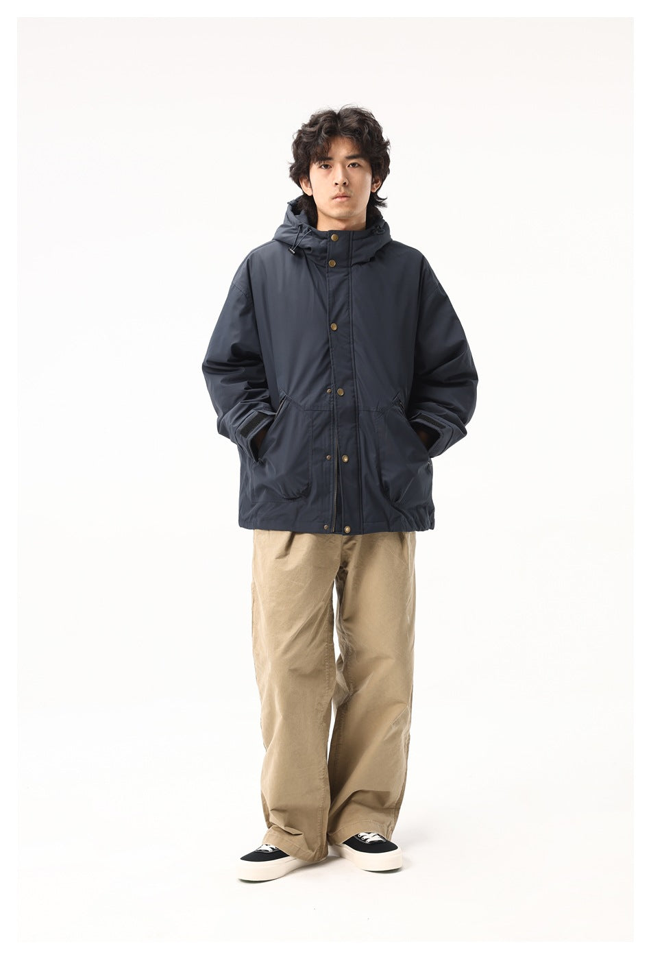 Full-length front view of a model wearing a dark navy hooded jacket with brass-tone snaps and tan trousers.