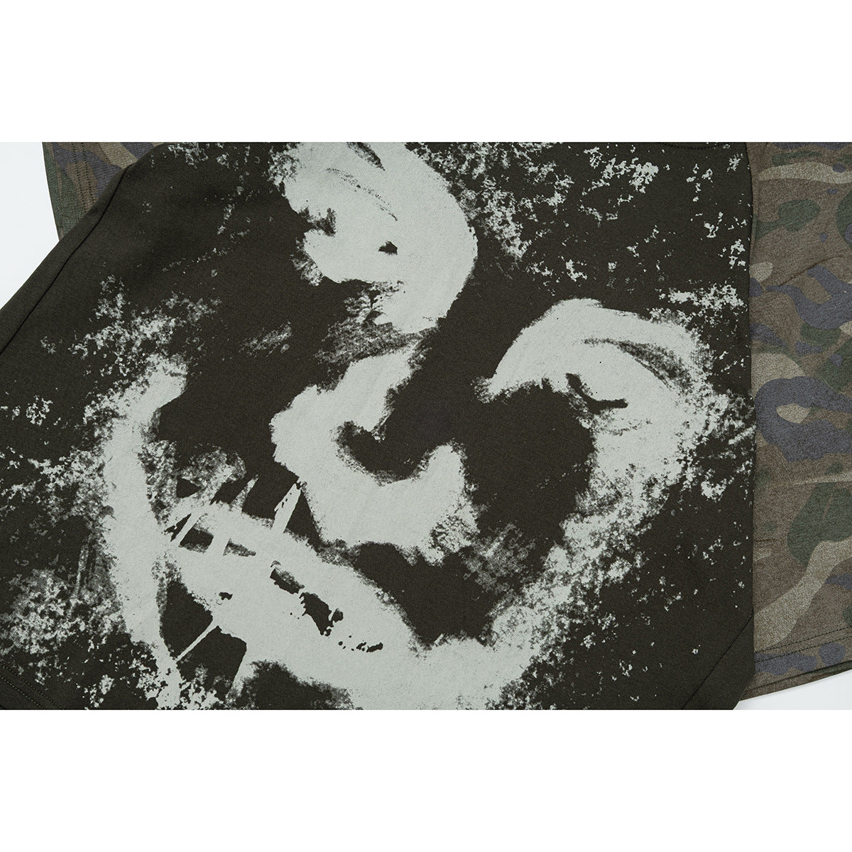 Close-up of a distressed light-colored graphic on the dark olive T-shirt front, beside a camouflage sleeve.