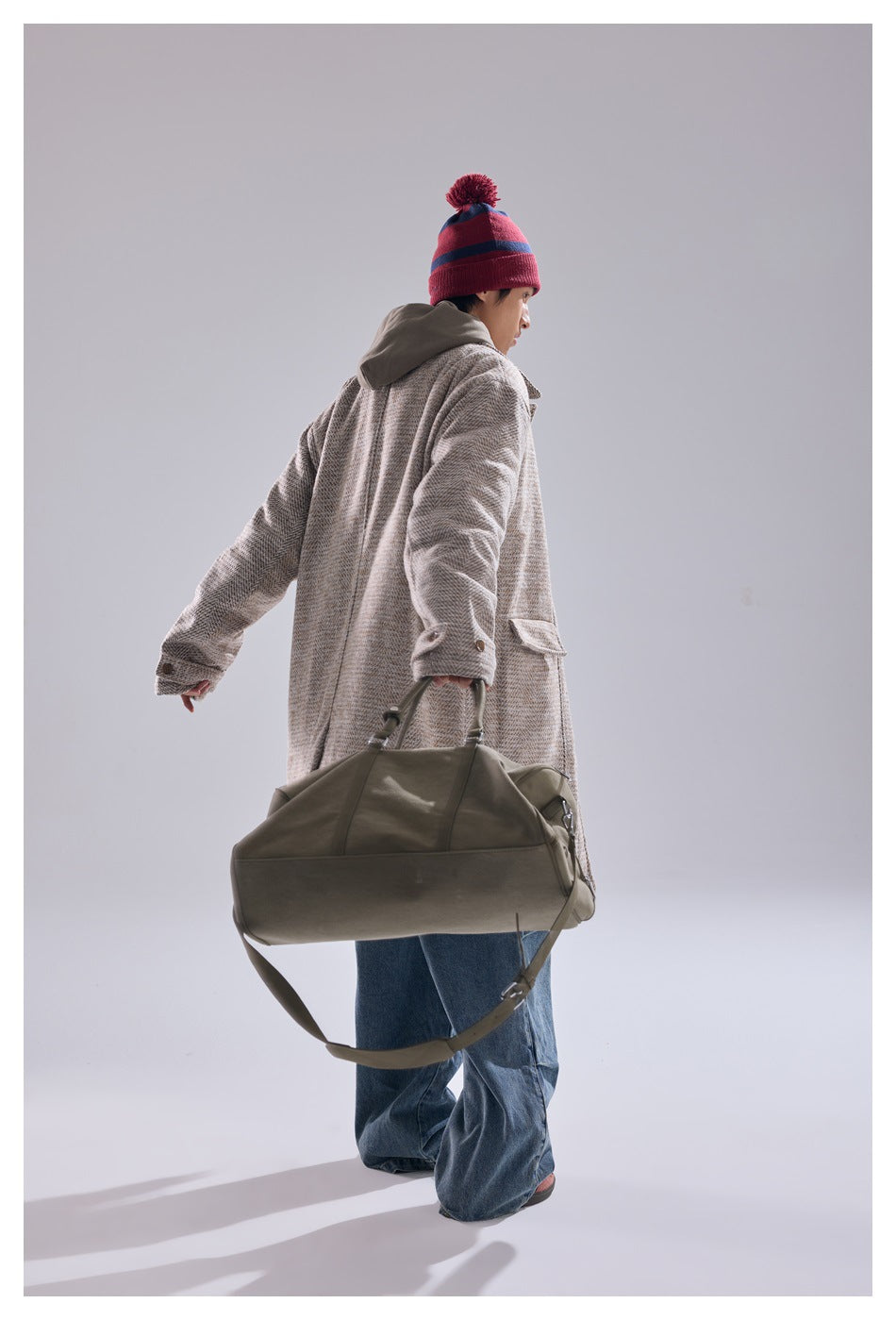 Model shown from behind wearing a beige herringbone coat and gray hood, carrying an olive duffel bag.