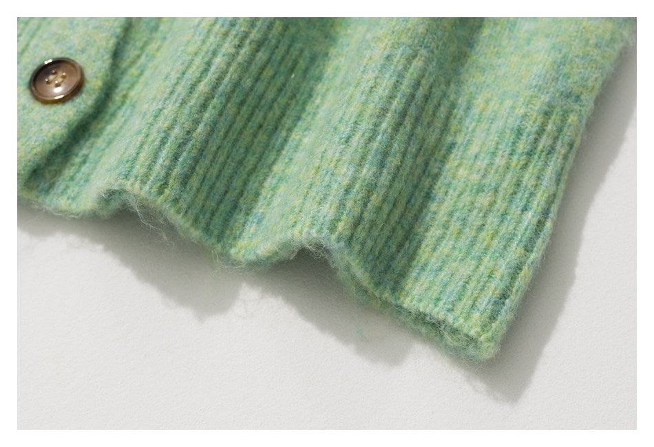 Close-up of a ribbed knit hem with a brown button on mottled mint-green fabric.
