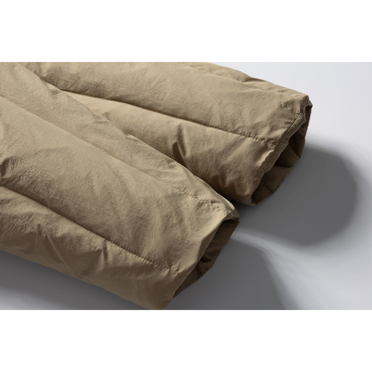 Close-up of tan padded jacket panels with stitched seams and a softly crinkled surface.