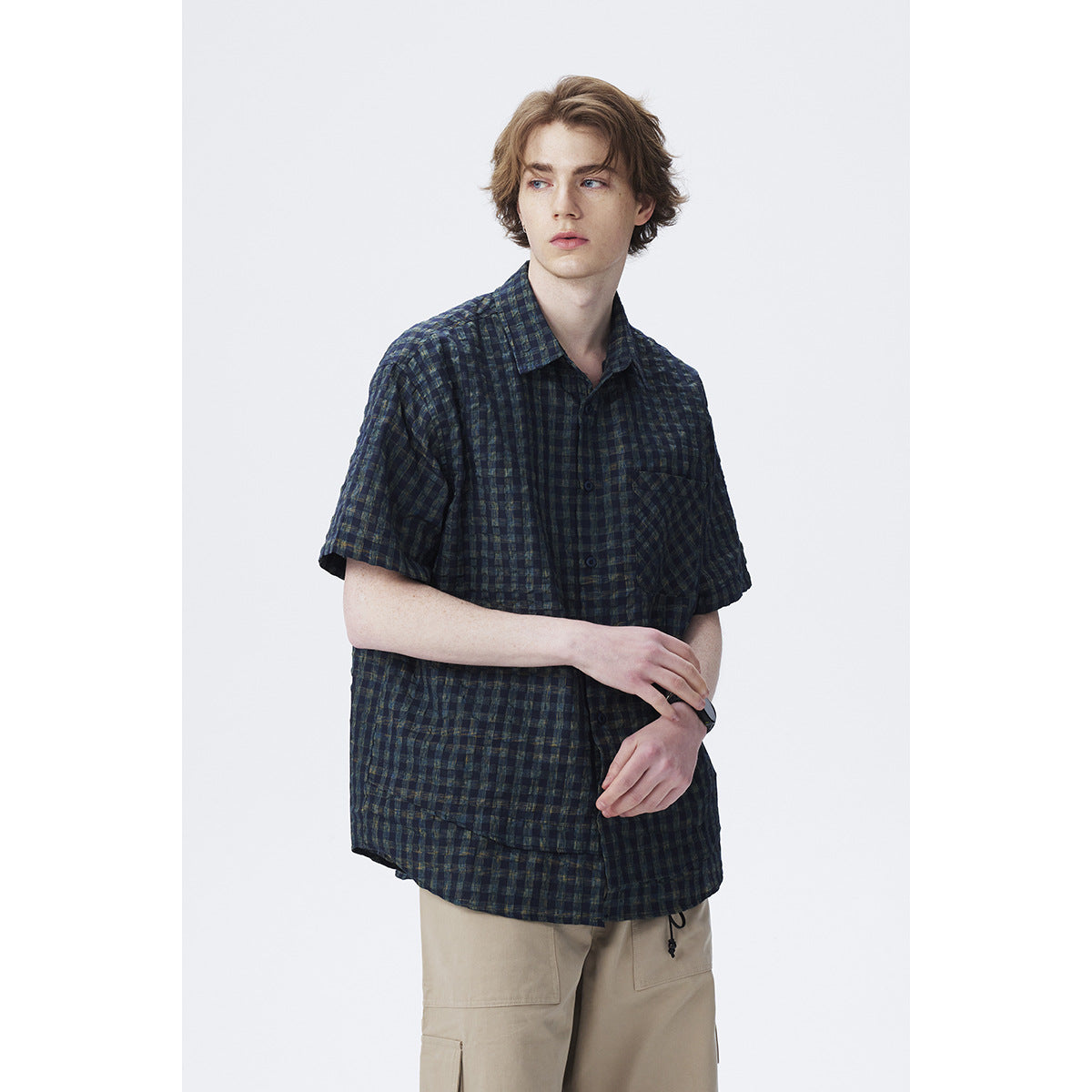 Model wearing a dark navy and green plaid short-sleeve button-up shirt with a chest pocket.
