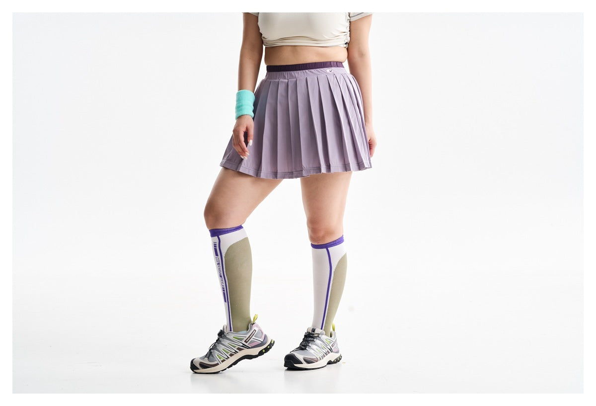 Model wearing a pleated lavender athletic skirt with a dark waistband, knee-high socks, and sneakers, shown from the front.