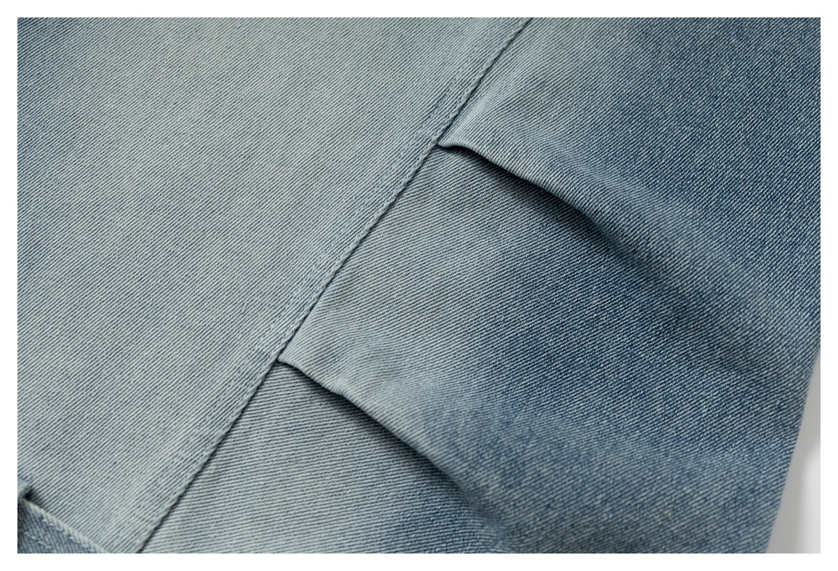 Close-up of layered blue denim panels with diagonal seams and a folded pleat.