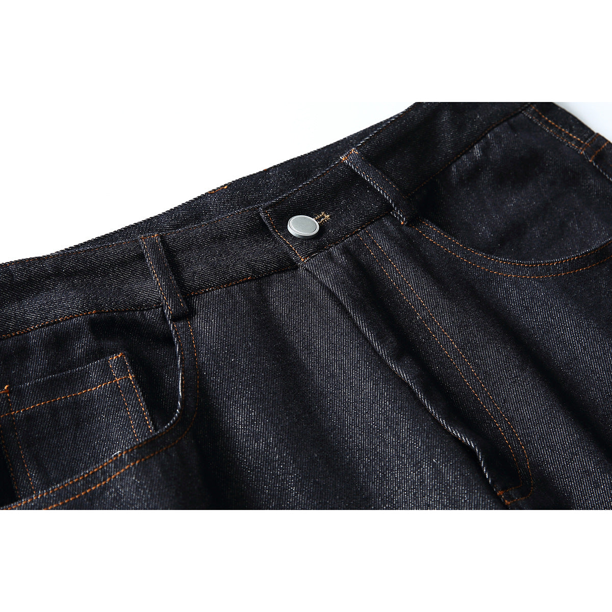 Close-up of dark indigo jeans showing the waistband, silver button, fly, belt loop and orange stitching.