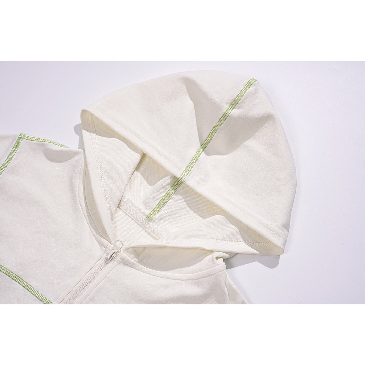 Close-up of an off-white zip hoodie’s hood and neckline, with lime-green contrast stitching.