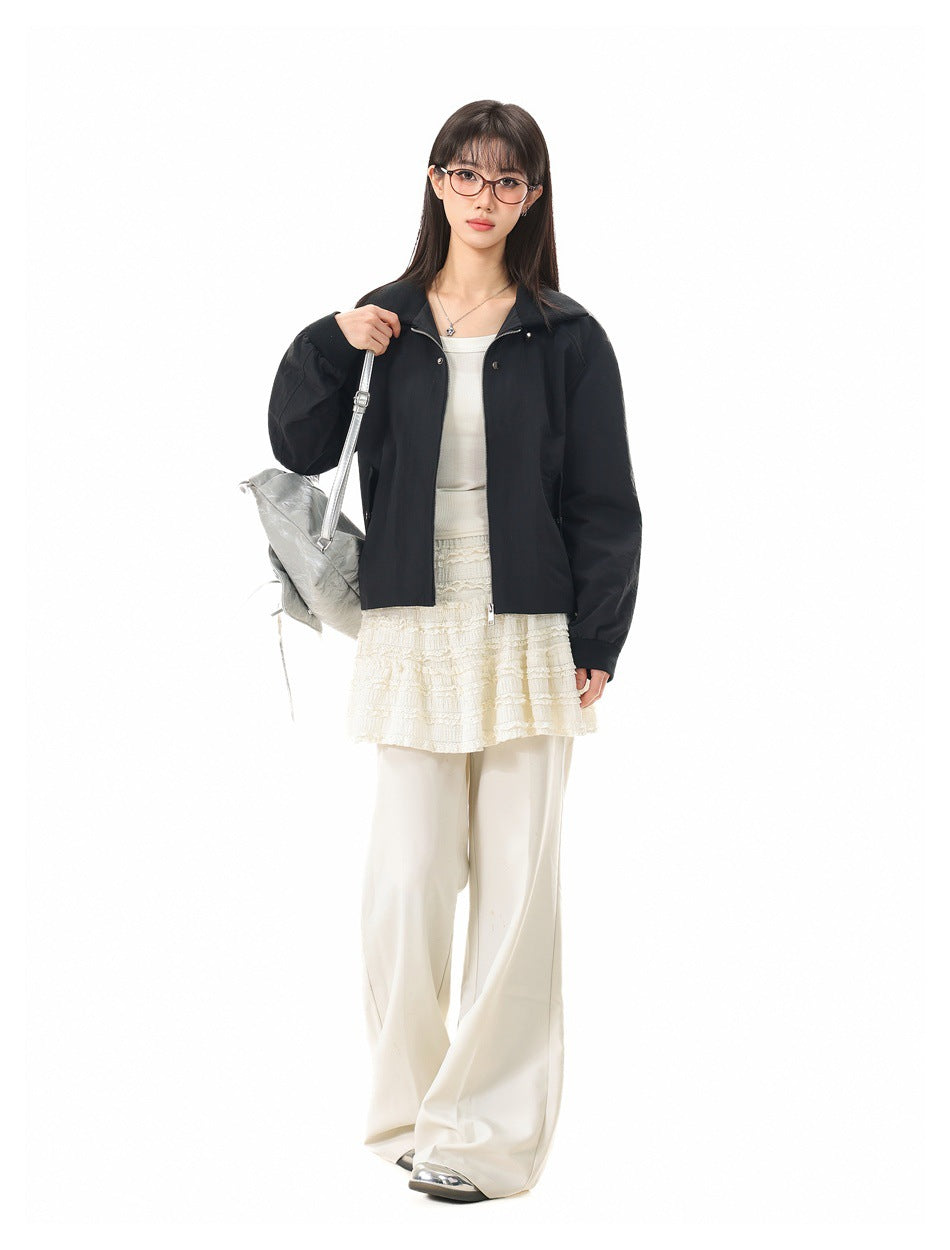 Model wearing a black collared zip jacket with a silver shoulder bag, cream lace top and wide-leg trousers.