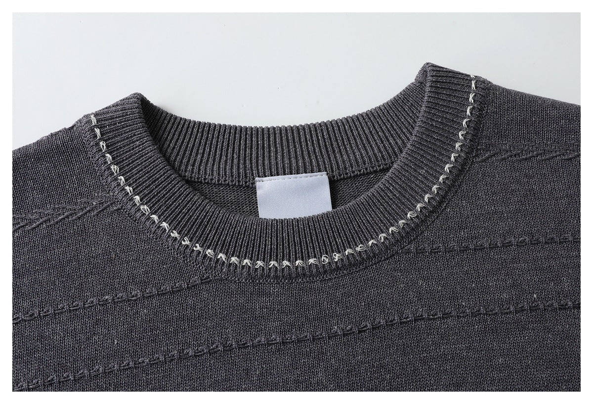 Close-up of a charcoal sweater's ribbed crew neckline with contrasting light loop stitching and horizontal decorative seams.
