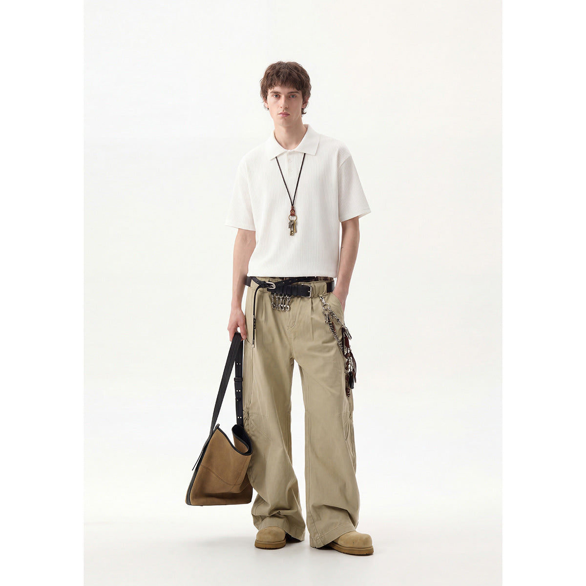 Full-length model wearing a white ribbed polo shirt and loose beige trousers with belts and chains.