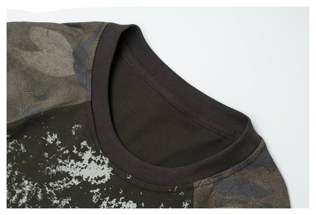 Close-up of the ribbed neckline, distressed front graphic, and camouflage shoulder panel on a dark olive T-shirt.