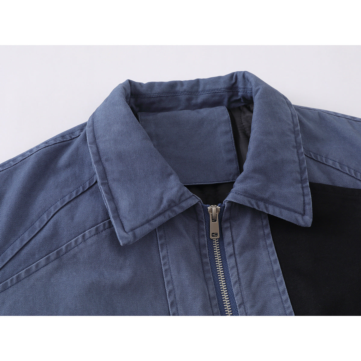 Close-up of a blue jacket's pointed collar, front zipper, shoulder seams and black chest panel.
