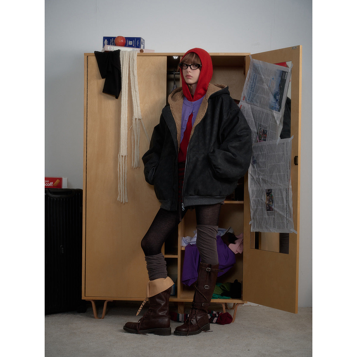 Model wearing an oversized black hooded jacket with tan lining, layered over a red hoodie and purple cardigan.