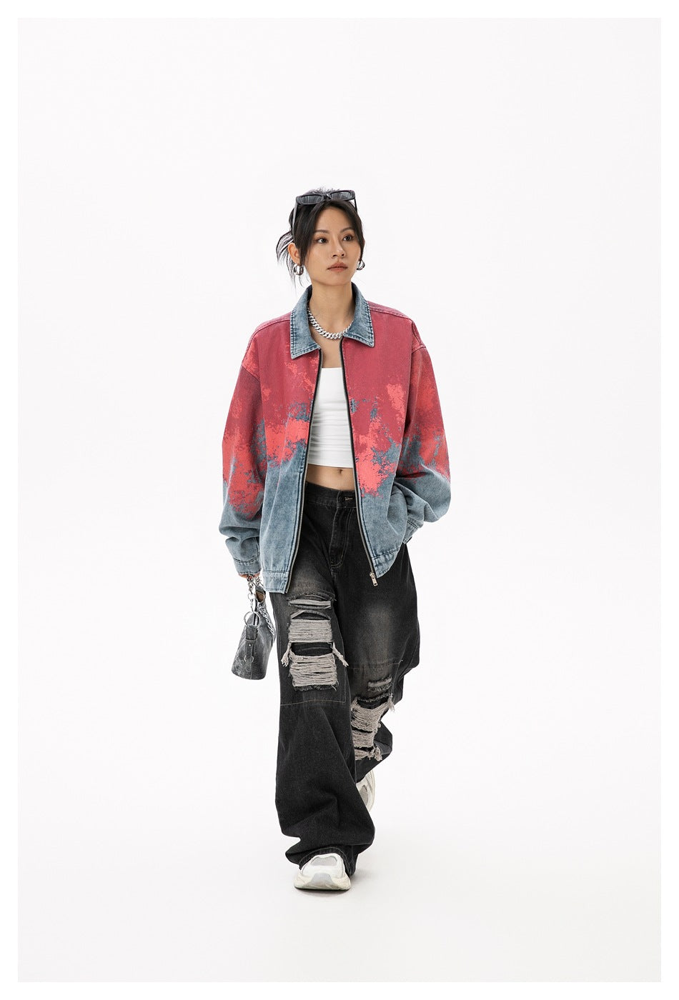 Model wearing an oversized blue denim zip jacket with coral-red mottled detailing and black ripped jeans, front view.