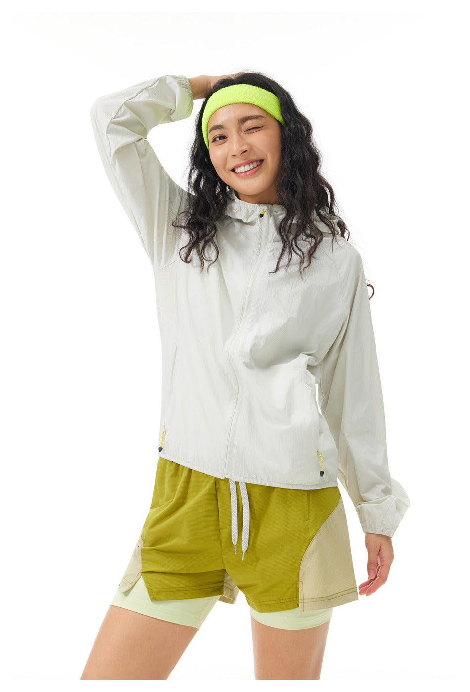 Model wearing an off-white hooded jacket and layered olive shorts, posing with one arm raised.