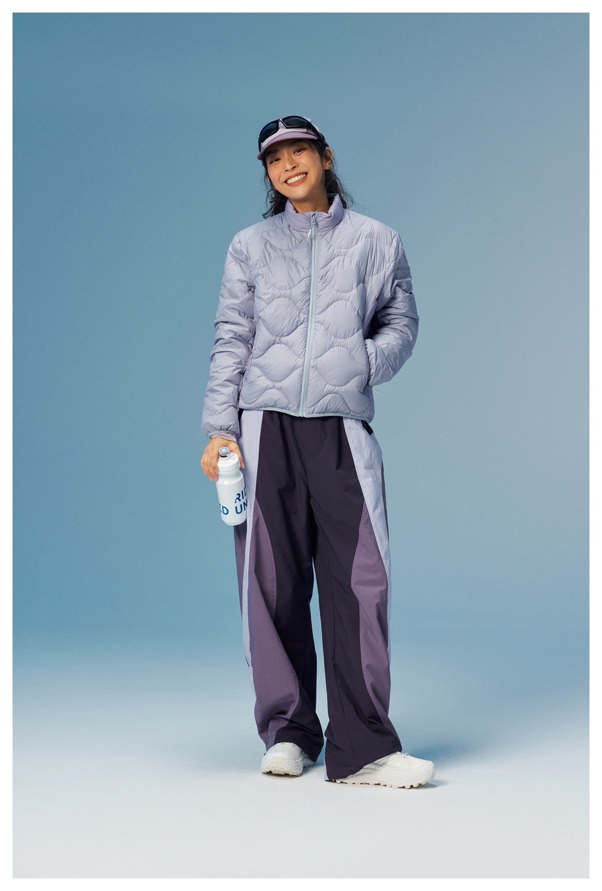 Full-length view of a woman in a pale lavender wave-quilted zip jacket and dark color-block wide-leg pants.