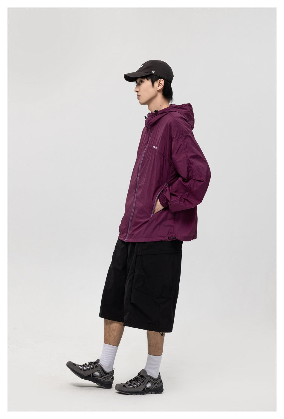 Side view of a model wearing a burgundy hooded jacket and black shorts.