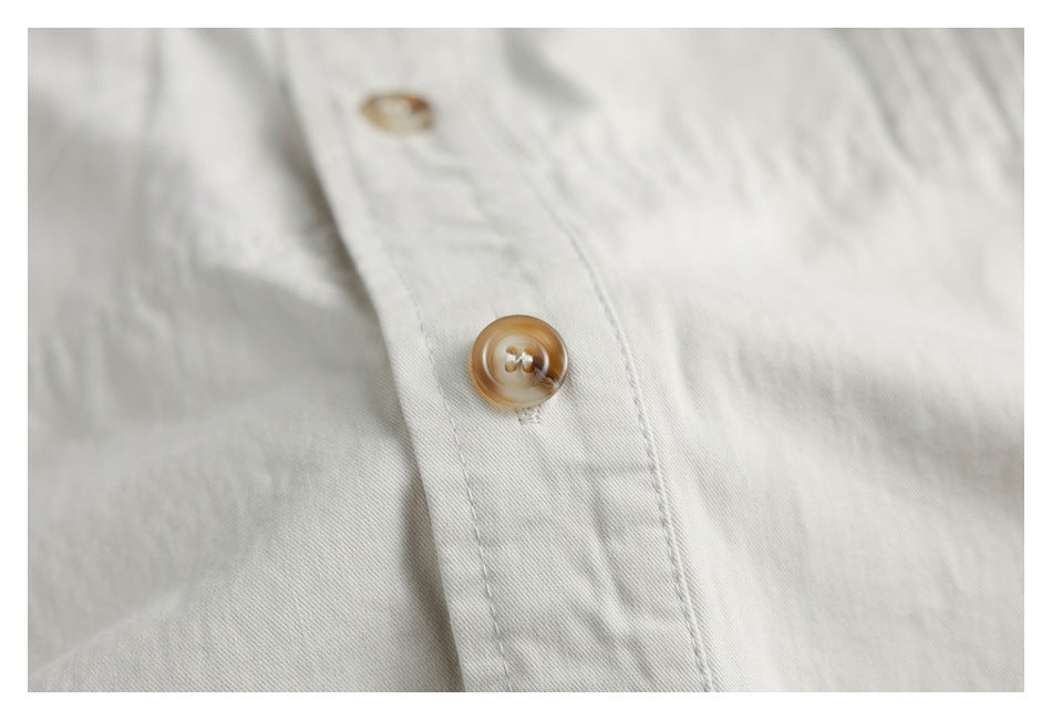 Close-up of a tan button on the off-white shirt's stitched front placket.