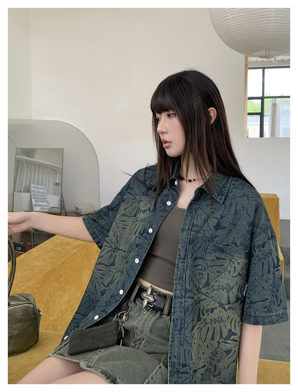 Model wearing an open, oversized blue-gray botanical-print shirt with short sleeves and a chest pocket.