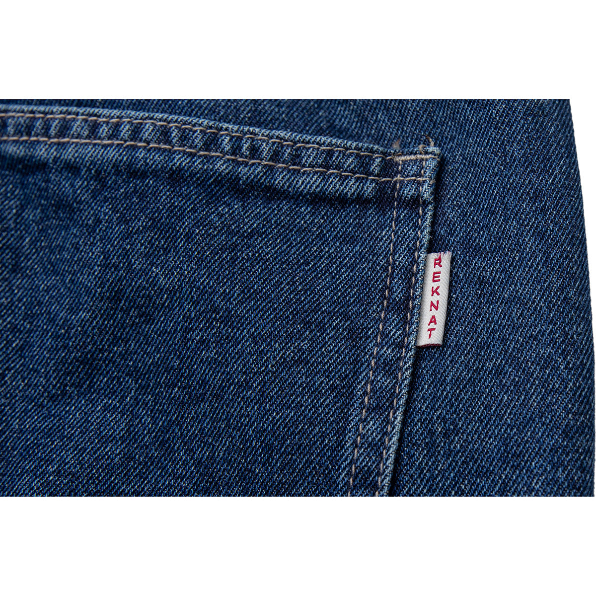 Close-up of dark blue denim stitching and a small white sewn tag with red lettering.