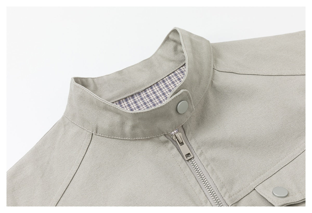 Close-up of a light beige jacket collar, plaid inner trim, snap button, and front zipper.