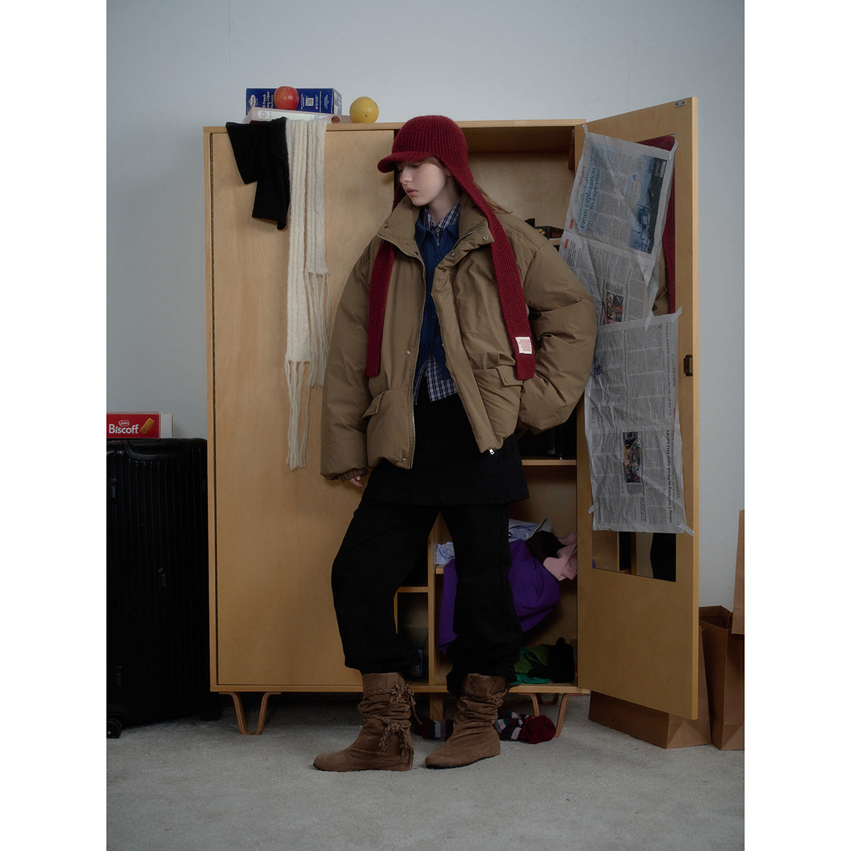 Model wears an oversized brown puffer jacket with black trousers and a burgundy knit hat and long scarf.