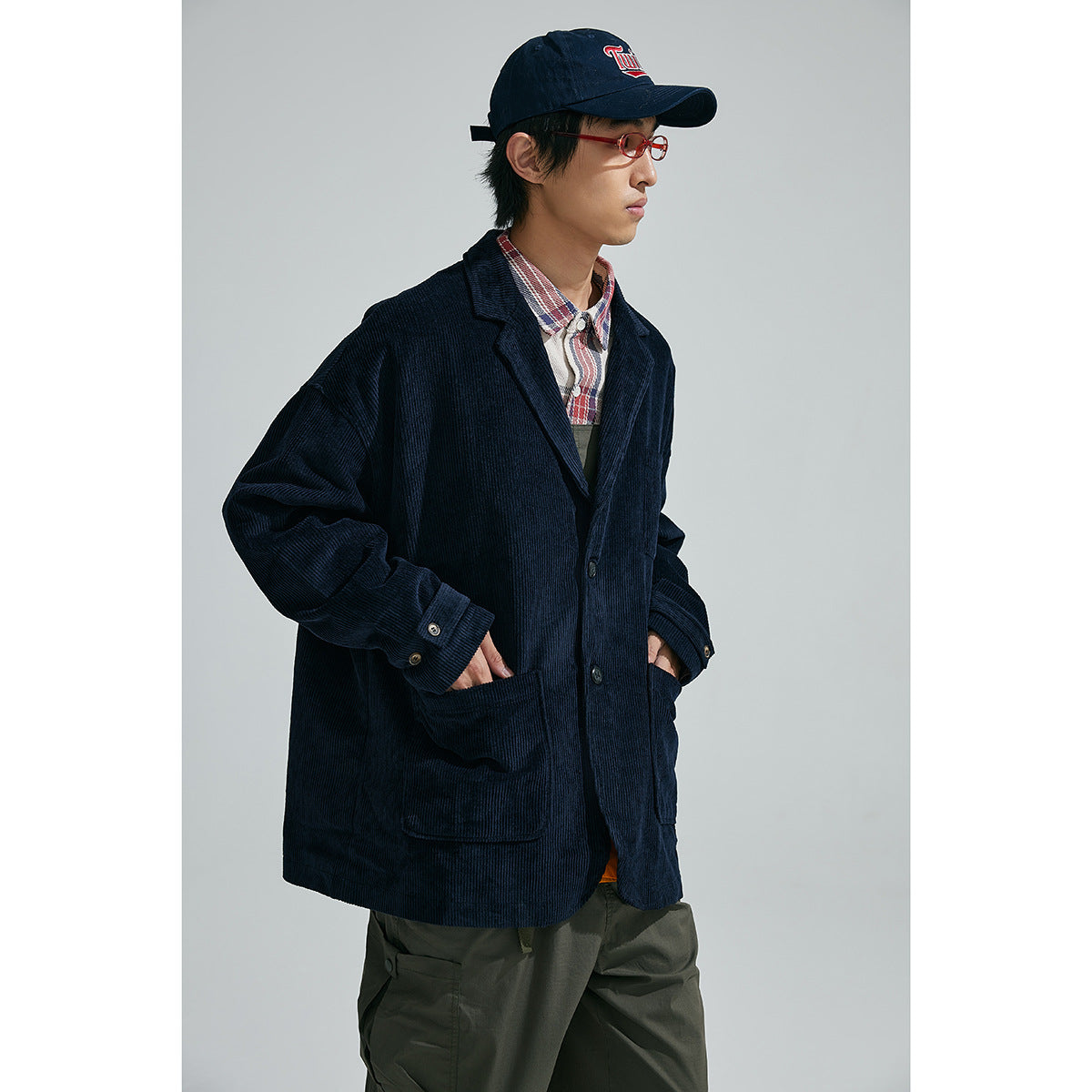 Model wearing an oversized dark navy ribbed blazer with large patch pockets, over a plaid shirt and dark trousers.