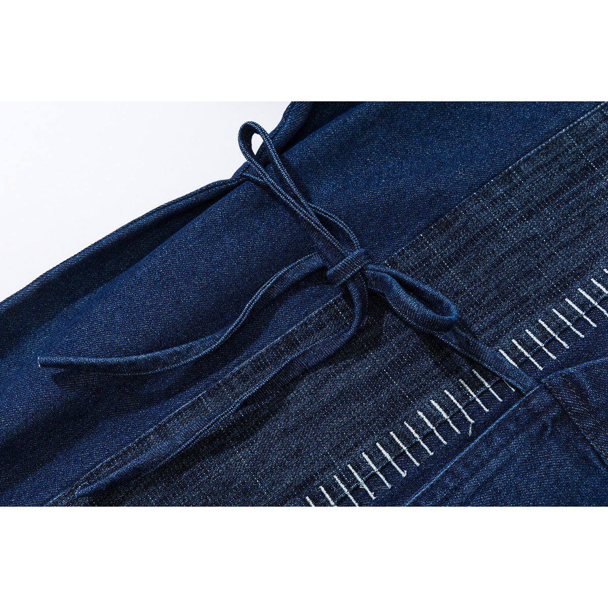 Close-up of a dark blue denim wrap jacket tie and white ladder-style stitching.