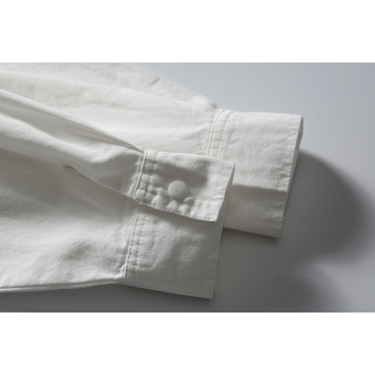 Close-up of a white shirt sleeve and cuff with a single white button.