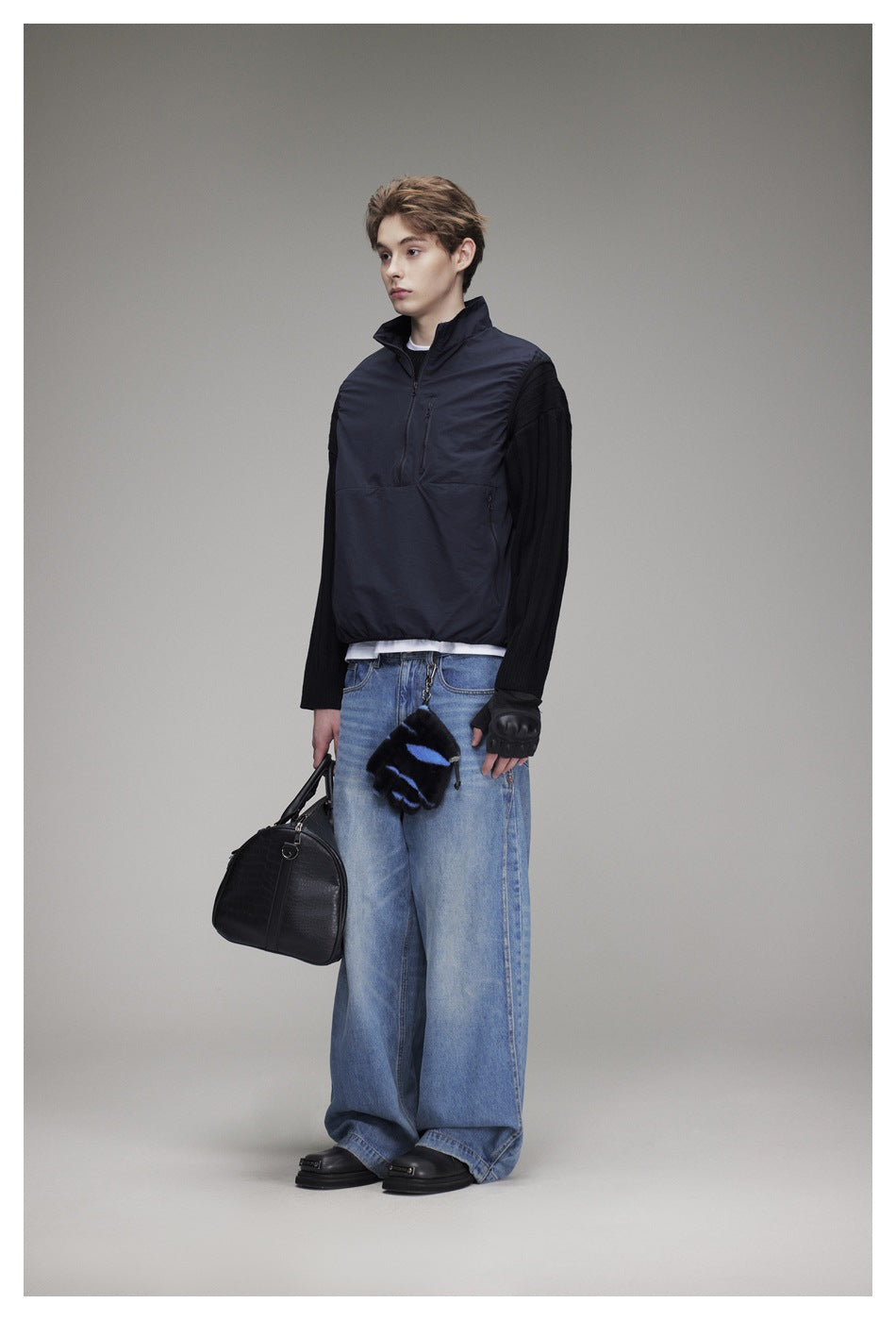 Model wearing a navy quarter-zip pullover with black ribbed sleeves and loose blue jeans.
