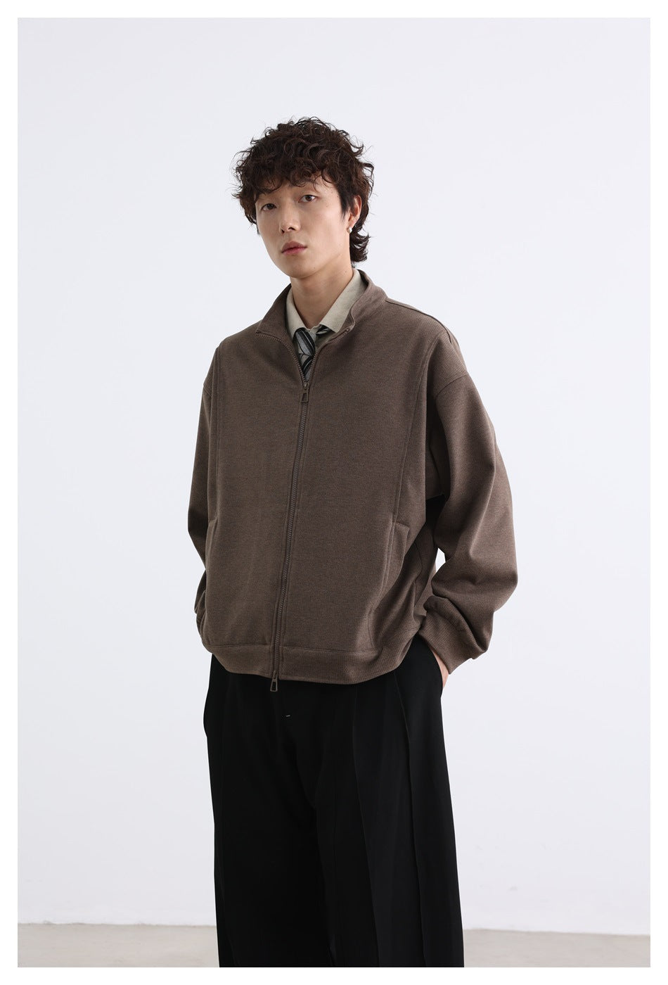Model wearing a brown zip-front jacket zipped closed, with a raised collar and front pockets.