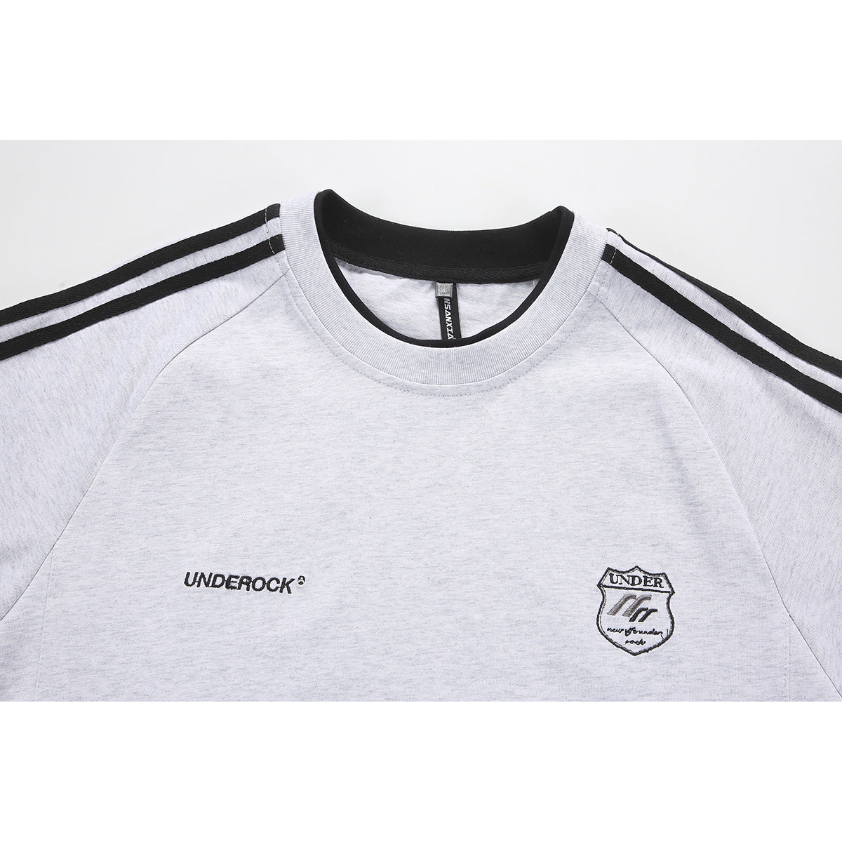 Close-up of a light gray T-shirt with black shoulder stripes, a black collar, and small chest logos.
