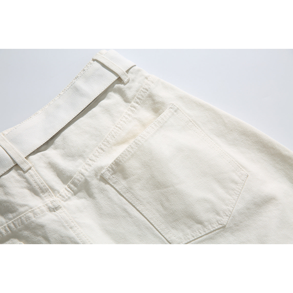 Close-up of the back of ivory shorts, showing a square patch pocket and belt loops.