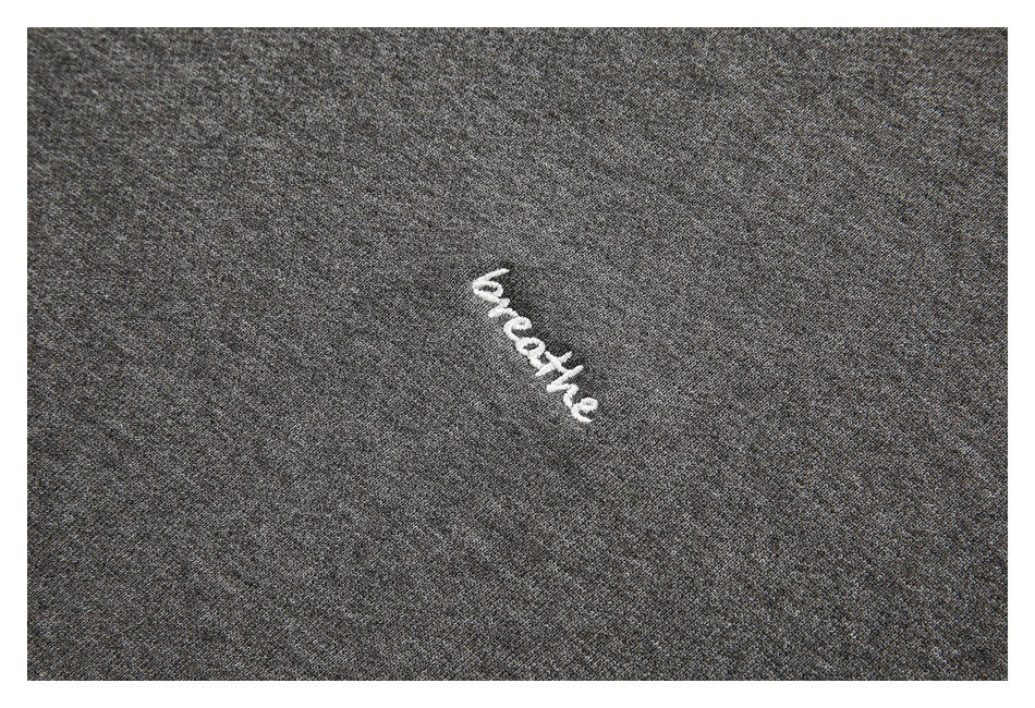 Close-up of white embroidered “breathe” lettering on charcoal gray sweatshirt fabric.