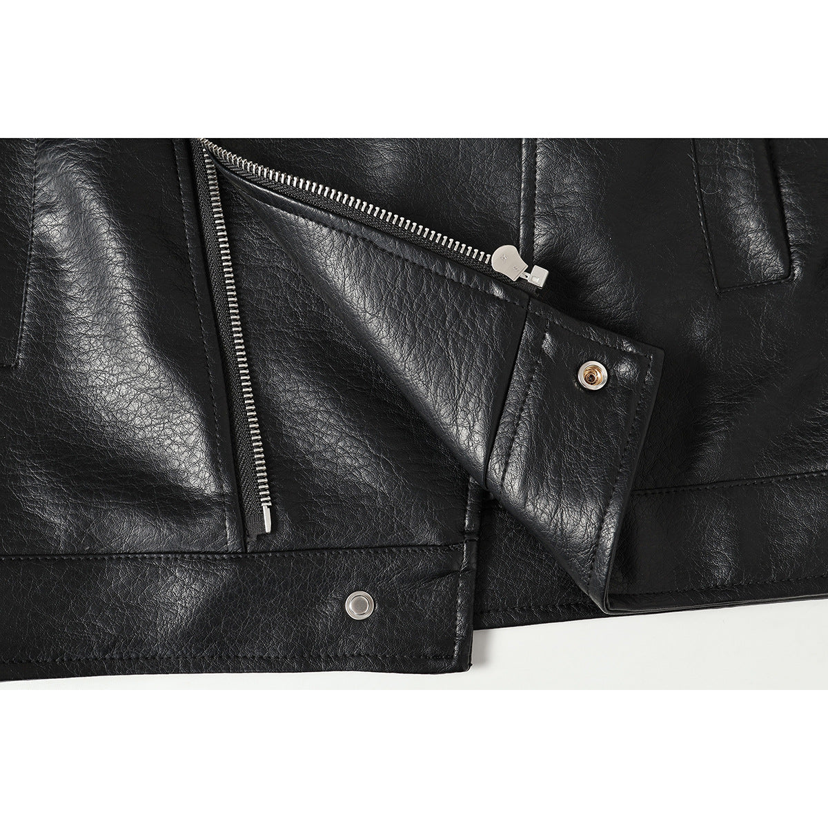 Close-up of a black jacket's diagonal silver zipper, snap-fastened lapel, and stitched hem.