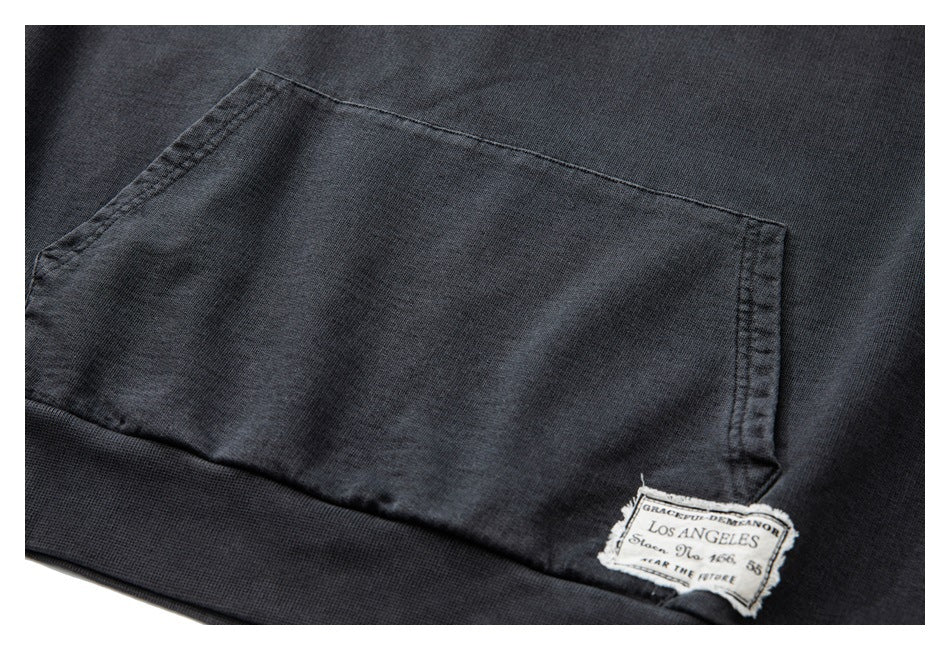 Close-up of a charcoal hoodie kangaroo pocket with a small sewn label near the ribbed hem.
