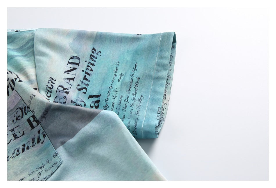 Close-up of the blue-green shirt's short sleeve and hem, showing the landscape-style print and English lettering.