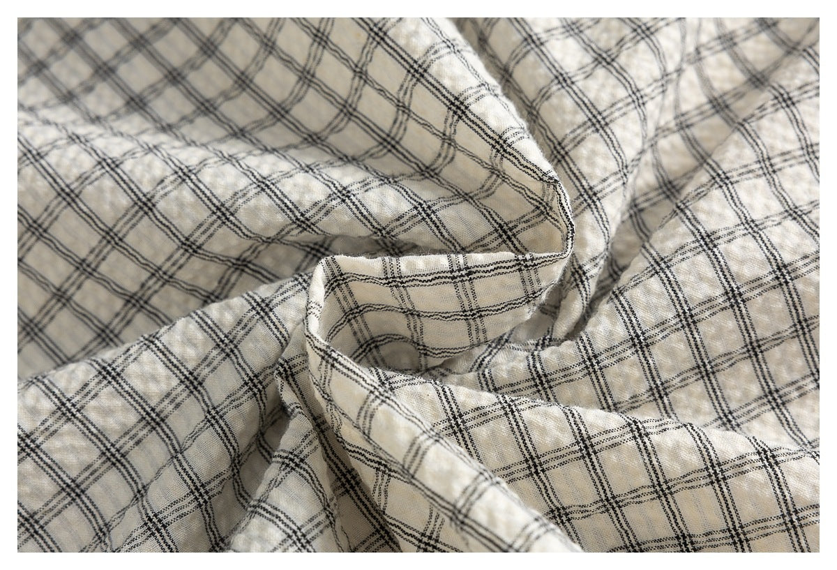 Draped cream fabric with a black plaid pattern, shown in a close-up of its folds.